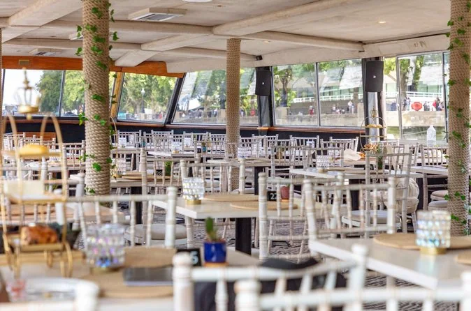 Rows of set tables in a boat's dining saloon with large windows on both sides