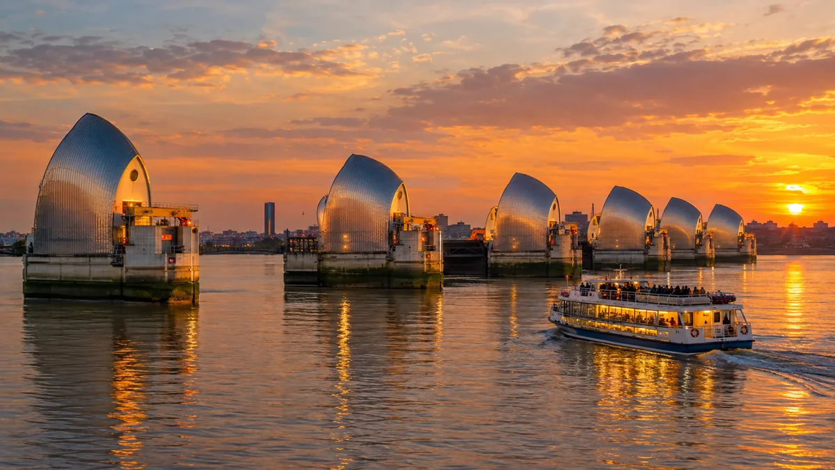 The steel hoods of the Thames Barrier at sunset with a cruise boat sailing past